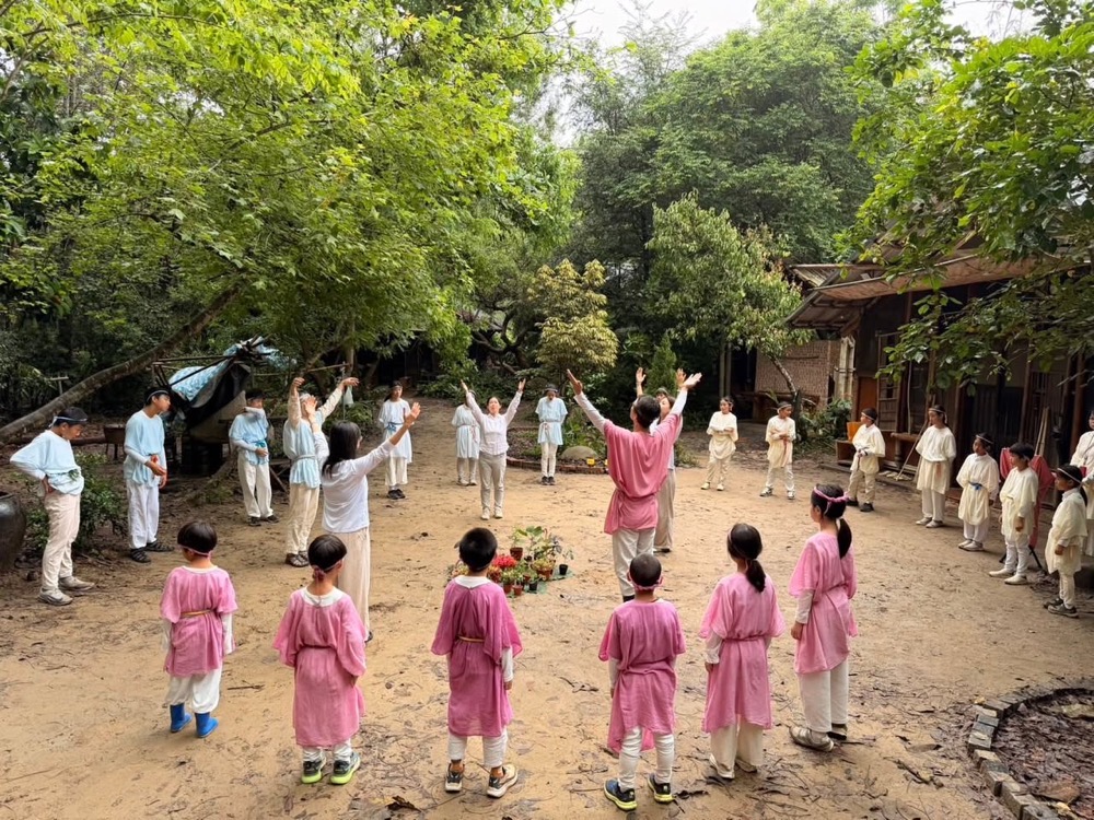 孩子們穿著粉色與白色的慶典服,在桃花心木林間圍成圓圈歌唱
